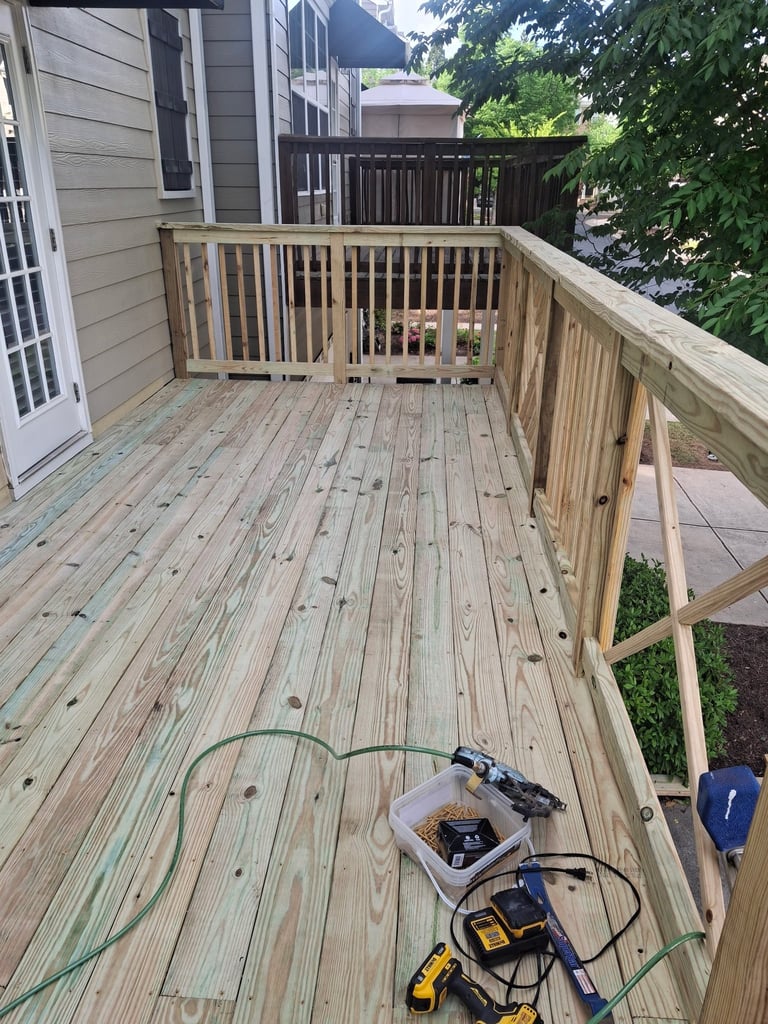 Wooden deck under construction with power tools and extension cord on the boards, wooden railings, and residential houses in background