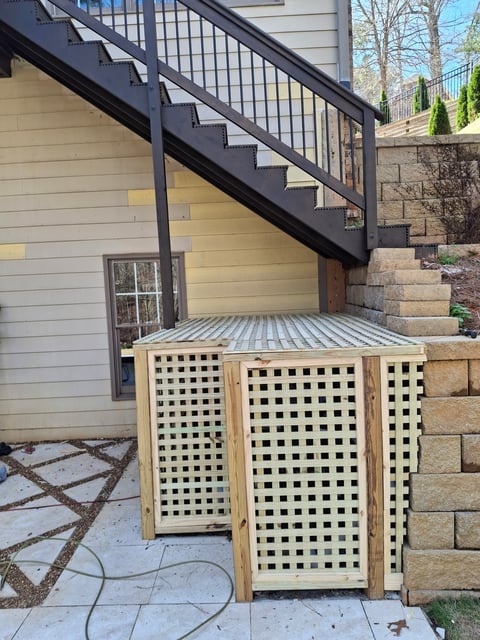 Wooden lattice trash enclosure under modern black metal staircase on patio