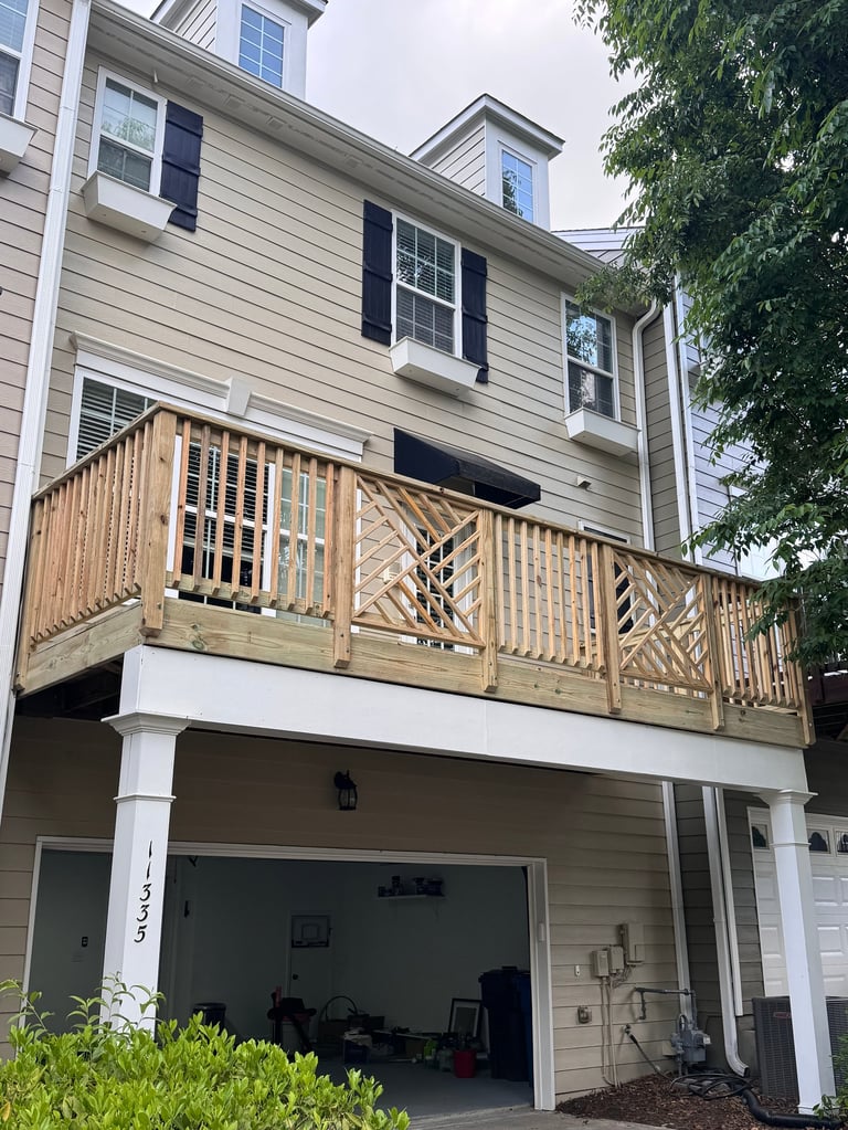 Two-story house with beige siding, black shutters, wooden deck railing, and attached garage below