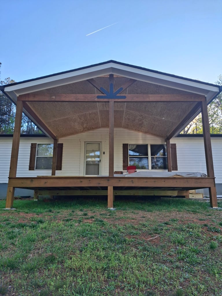 Single-story white house with wooden front porch awning and cross decoration, elevated on posts above grass