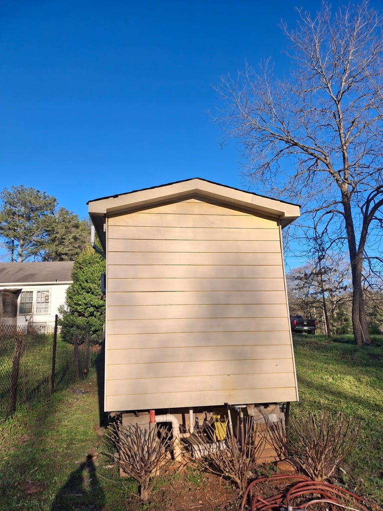 Beige prefab shed with gabled roof in residential yard with bare trees under clear blue sky